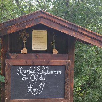 A traditional wooden sign with the inscription "Warm Welcome to the Ötztal". Surrounded by green trees and a rural setting. | © Nicole Lughammer
