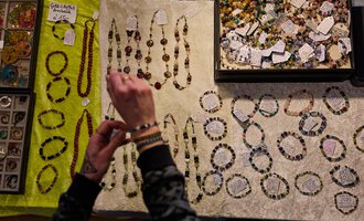 Ein Standsort mit verschiedenen Schmuckstücken aus Perlen und Steinen. Eine Person betrachtet die Halsketten und Armbänder auf einem hellen Tuch.