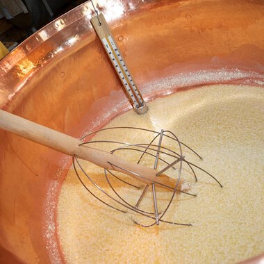 In a large copper kettle, a mixture is prepared. A wooden stirrer is dipped into the golden mass.