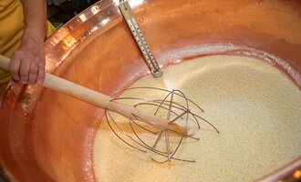 In a large copper kettle, a mixture is prepared. A wooden stirrer is dipped into the golden mass.