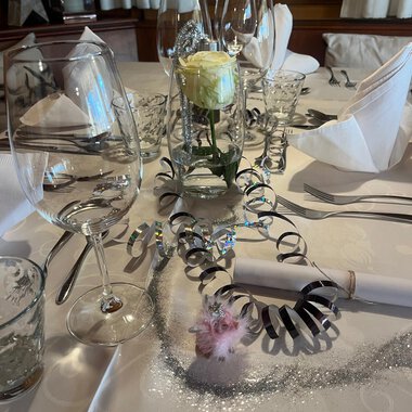 Two champagne glasses toast on a festively decorated table. In the background, red Christmas ornaments and golden decorations can be seen. | © Genuss- & Aktivhotel Sonnenburg