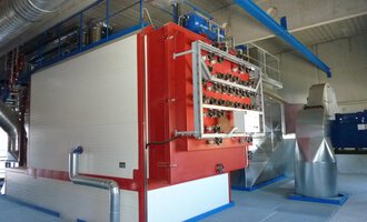 Eine moderne industrielle Anlage mit großen Maschinen und Rohren. Die Hauptmaschine ist rot und weiß, umgeben von einer strukturierten Umgebung.