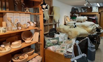 Ein gemütlicher Laden mit Holzregalen voller Handwerksprodukte. Im Hintergrund liegen hochwertige Wollprodukte und Dekorationen. | © Abler Mitbringsel Riezlern | Veronika Senn