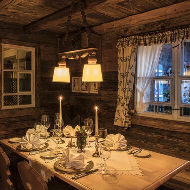 A cozy restaurant with a beautifully set table. The warm lights and wooden walls create an inviting atmosphere. | © Alpahotel Walserstuba GmbH Patrik Säly Photography