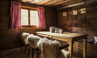 A cozy room with a wooden table and soft chairs. Red window frames and wood paneling create a warm atmosphere. | © Kleinwalsertal Tourismus | Oliver Farys