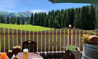 Ein gemütlicher Außenbereich mit einem Tisch und Getränken. Im Hintergrund ist eine schöne, grüne Landschaft mit Wald und Bergen zu sehen. | © Alpenhotel DAS KÜREN