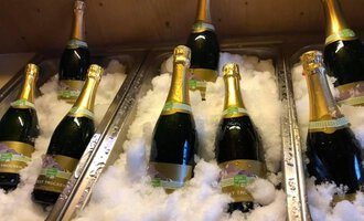 Six bottles of sparkling wine are lying in an ice bucket. The bottles are adorned with golden caps and labels.