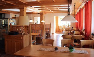 Ein gemütliches Restaurant mit Holzinterieur und großen Fenstern. Rote Vorhänge und gut eingedeckte Tische schaffen eine einladende Atmosphäre.