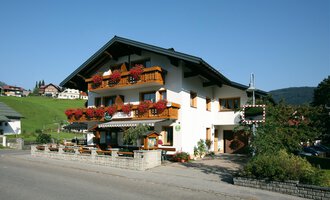 Ein malerisches Gebäude im alpinen Stil mit blühenden Balkonen. Es liegt in einer ruhigen, grünen Umgebung. | © Cafe Jochum | Bernadette Reinmuth