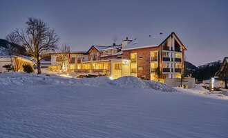 A cozy hotel in a snowy landscape. The lights of the building shine in the twilight. | © Genuss- & Aktivhotel Sonnenburg | Alexander Kais