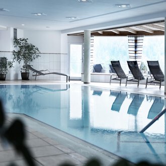 A bright indoor pool with loungers and plants. The room is designed to be modern and inviting. | © Hotel Birkenhöhe