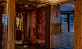 A modern reception area with wooden elements and large glass surfaces. The cozy atmosphere is enhanced by warm lighting and tasteful decorations. | © IFA Hotel Alpenhof Wildental | Andreas Froschauer