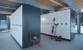 A modern ski room with white lockers and a red chair. Ski equipment and a helmet are on the wall. | © Sport Kessler GmbH