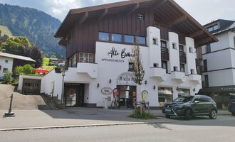 Ein modernes Gebäude mit Holz- und Putzfassade, das Apartments anbietet. Im Hintergrund sind grüne Berge und ein blauer Himmel zu sehen. | © Kleinwalsertal Tourismus | N. Lughammer