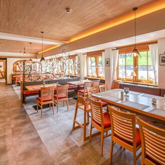 Ein modernes Restaurant mit Holzmöbeln und einer einladenden Atmosphäre. Große Fenster lassen viel Tageslicht herein und bieten einen Blick ins Freie. | © Familienhotel Kleinwalsertal Hotelgesellschaft mbH