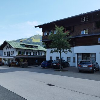 Ein ruhiges Dorf mit traditionellen Häusern und Autos auf der Straße. Im Hintergrund sind grüne Hügel sichtbar. | © Kleinwalsertal Tourismus | Nicole Lughammer