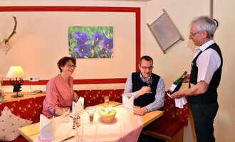 A stylish restaurant with a cozy atmosphere. A waiter is serving a couple at the table a bottle of wine. | © IFA Breitach Apartements