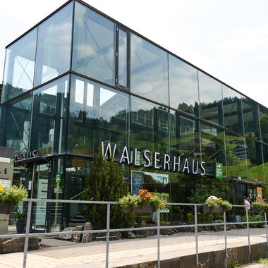 A modern building called Walserhaus in a mountainous environment. Surrounded by trees and under a clear sky. | © Kleinwalsertal Tourismus | Oliver Farys