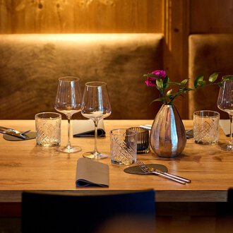 A beautifully set table in a cozy restaurant. It is decorated with glasses, cutlery, and a vase of flowers. | © La Vallée | Annette Sandner