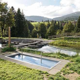 A small pool in a green environment with trees and a calm water surface in the background. The landscape is gently rolling and invites relaxation. | © Kleinwalsertal Tourismus | Veronika Senn