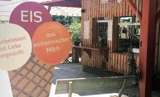 A cozy ice cream parlor with wooden paneling and a counter area. In the foreground, there is a large ice cream sign that indicates homemade ice cream. | © PAPILLON EISDIELE | Eis & Crêpe | Lisa Schüttler