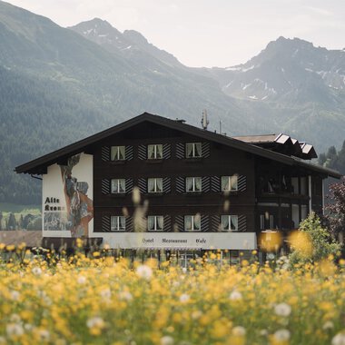 A traditional building in a picturesque landscape. In the foreground, yellow wildflowers are blooming, while the mountains are visible in the background.