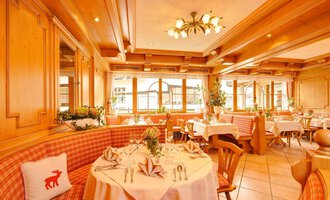 Ein gemütliches Restaurant mit Holzwänden und eleganten Tischdecken. Die Atmosphäre wird durch natürliche Lichtquellen und dekorative Pflanzen belebt. | © Aparthotel Kleinwalsertal Haller GmbH & Co KG