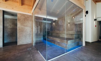 A modern sauna area with glass walls and stylish stone benches. The soft lighting creates a relaxing atmosphere.