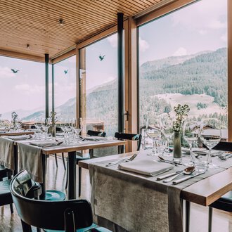 Ein modernes Restaurant mit großen Fenstern und Blick auf die Berge. Die Tische sind elegant gedeckt und schaffen eine einladende Atmosphäre. | © Naturhotel Chesa Valisa | Heldentheater