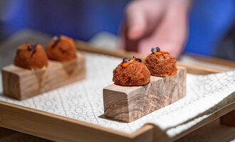 A stylish presentation of small delicacies on a wooden platter. The bite-sized treats are decorated with colorful accents.