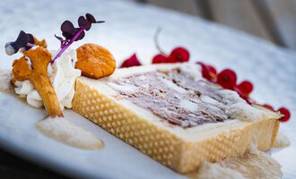 An artfully arranged dessert on a white plate. It consists of a rectangular shape, garnished with edible flowers and fruits.