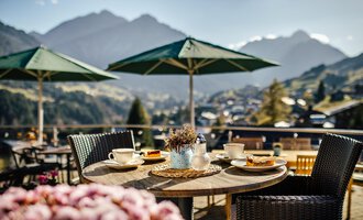 A beautiful table outdoors with a view of the mountains. On the table are coffee, pastries, and a small vase with lavender.