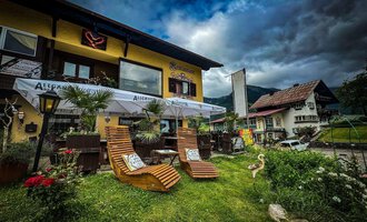 A cozy café with an inviting outdoor area. Two lounge chairs are situated on a green lawn, surrounded by plants and with a view of a charming building. | © Ristorante Monte Zaferna | K. Harmat-Hegedüs