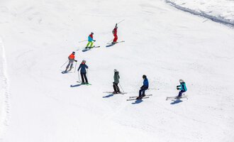 A group of skiers is standing on a snowy slope. The sky is clear and the sun is shining. | © Skischule Bödmen-Baad GmbH