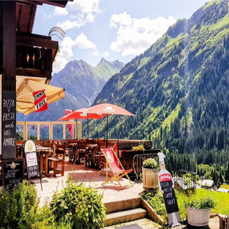 A cozy restaurant with outdoor seating and a view of the mountains. The surroundings are green and picturesque, ideal for a relaxing break. | © Starzelhaus Pizzeria La Marmotta | J. Reich-Ulicny