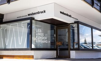 A modern printing house with a clear entrance. The sign shows the name "walserdruck" and the inscription "FAVORITE CUSTOMER ENTRANCE". | © Walserdruck KG