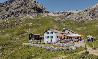 Ein malerisches Bergrestaurant umgeben von grünen Wiesen und Bergen. Der klare Himmel bietet eine schöne Kulisse für den Ort. | © Widdersteinhütte  | Vanessa Wüstner