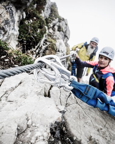 Two climbers with helmets and safety gear on a via ferrata climbing a rock face | © Kleinwalsertal Tourismus eGen • Photographer: Dominik Berchtold