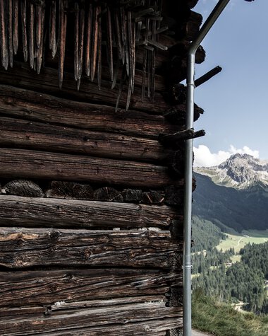 View of a wooden barn in the mountains with green valleys and peaks in the background under a sunny sky. | © Kleinwalsertal Tourismus eGen • Photographer: Dominik Berchtold