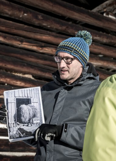 A man shows a historical photograph to a group during a cultural tour in winter. | © Kleinwalsertal Tourismus eGen • Photographer: Dominik Berchtold