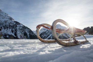 Skier und Rodel auf schneebedeckten Bergen im Winter, Sonnenlicht scheint durch die Berge. | © Kleinwalsertal Tourismus eGen • Fotograf: Dominik Berchtold