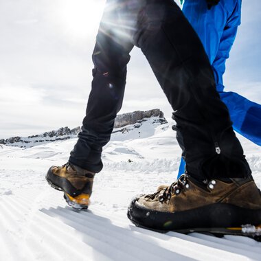 Close-up of two people winter hiking with mountain boots on snow, focusing on the shoes and legs in a winter landscape. | © Kleinwalsertal Tourismus eGen • Photographer: Dominik Berchtold