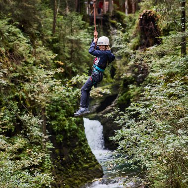 Junge Person beim Ziplining über einen Bach in einem grünen Wald im Kleinwalsertal. | © Kleinwalsertal Tourismus eGen • Fotograf: Oliver Farys