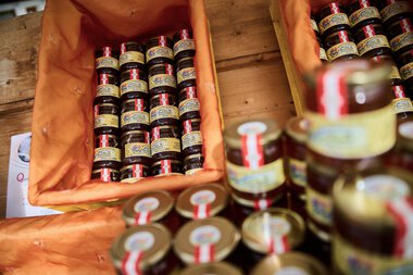Multiple jars of jam are in an orange box at a market stall. | © Kleinwalsertal Tourismus eGen • Photographer: Oliver Farys
