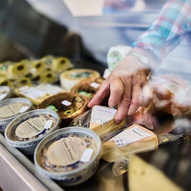 Hand selecting cheese at a stall display during the Walser Weekly Market in Kleinwalsertal. | © Kleinwalsertal Tourismus eGen • Photographer: Oliver Farys