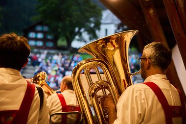Brass band performing outdoors with an audience in the background. The musicians are dressed in traditional costumes. | © Kleinwalsertal Tourismus eGen • Photographer: Oliver Farys