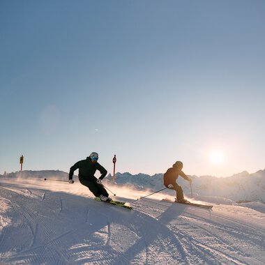Two skiers racing down a snowy slope in sunlight at Kleinwalsertal, Austria. | © Kleinwalsertal Tourismus eGen • Photographer: Oliver Farys