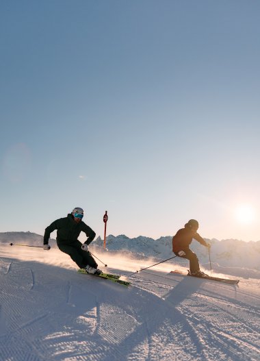 Zwei Skifahrer beim Rennen auf einer verschneiten Piste im Sonnenlicht in Kleinwalsertal, Österreich. | © Kleinwalsertal Tourismus eGen • Fotograf: Oliver Farys