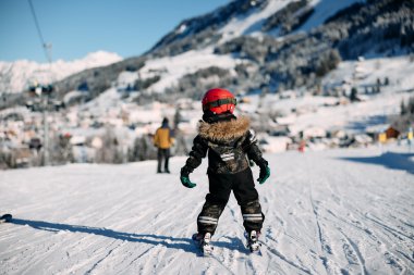 A child skier in winter clothing on a snowy slope, with mountains and other skiers in the background. | © Kleinwalsertal Tourismus eGen • Photographer: Oliver Farys