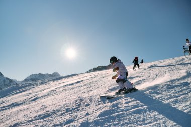 Child skiing on a snowy slope on a sunny day, with other children in the background and mountains in the distance. | © Kleinwalsertal Tourismus eGen • Photographer: Oliver Farys